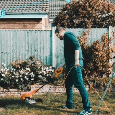 Small yard landscape ideas. man holding orange electric grass cutter on lawn